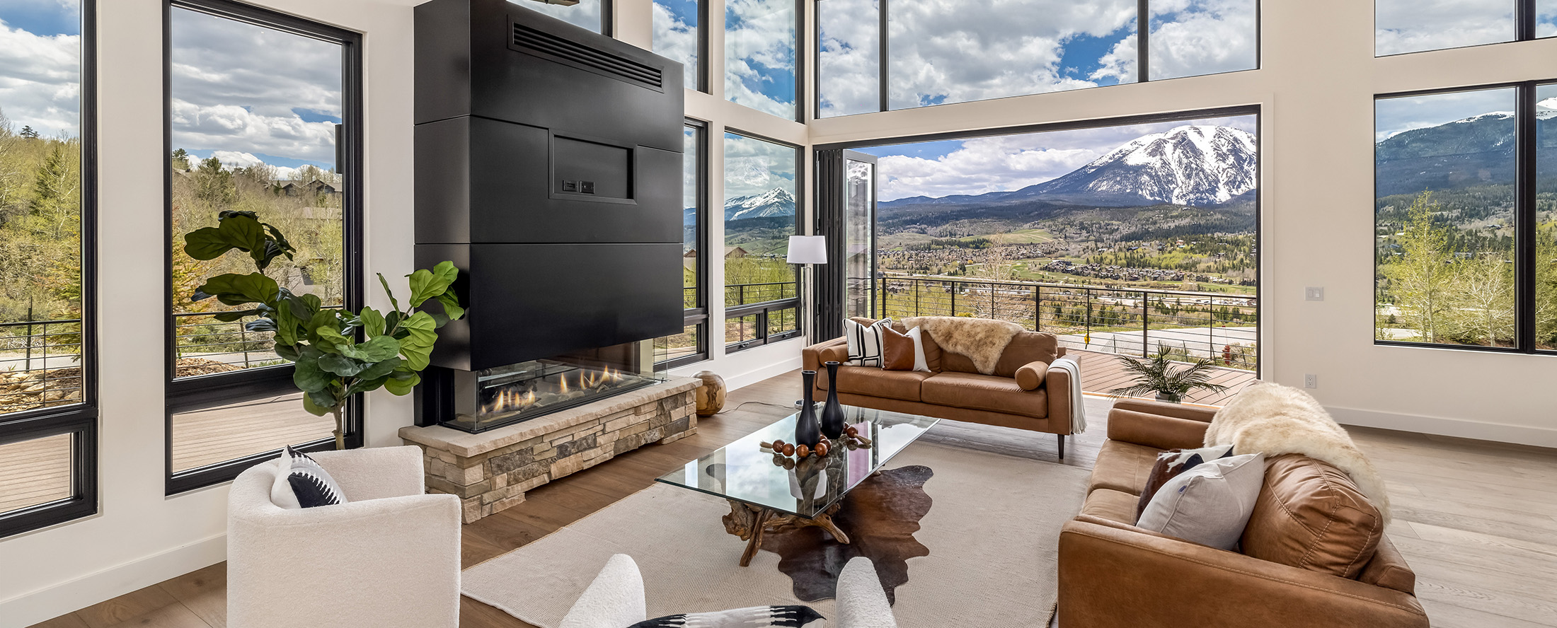 Luxury mountain modern great room with floor-to-ceiling windows, contemporary fireplace, and panoramic mountain views